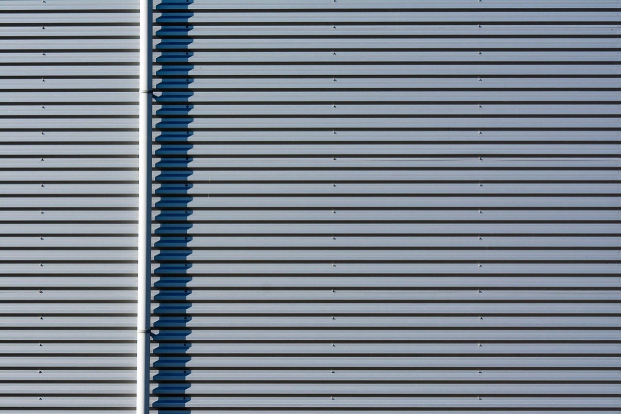 A corrugated grey metal facade with one dark blue joint running down it