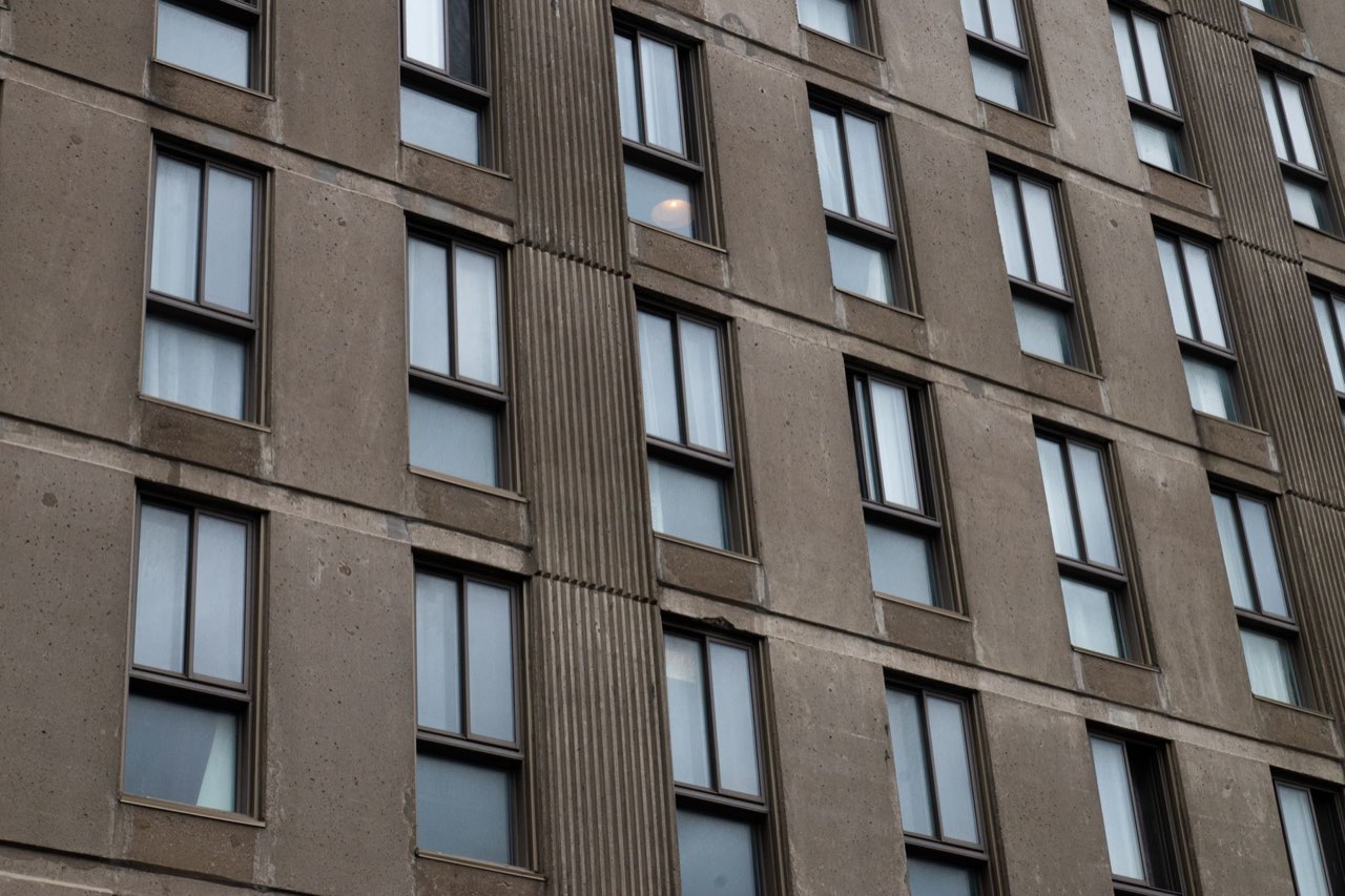 A brown concrete office facade seen at an angle, identical windows repeating across four floors between ribbed panels