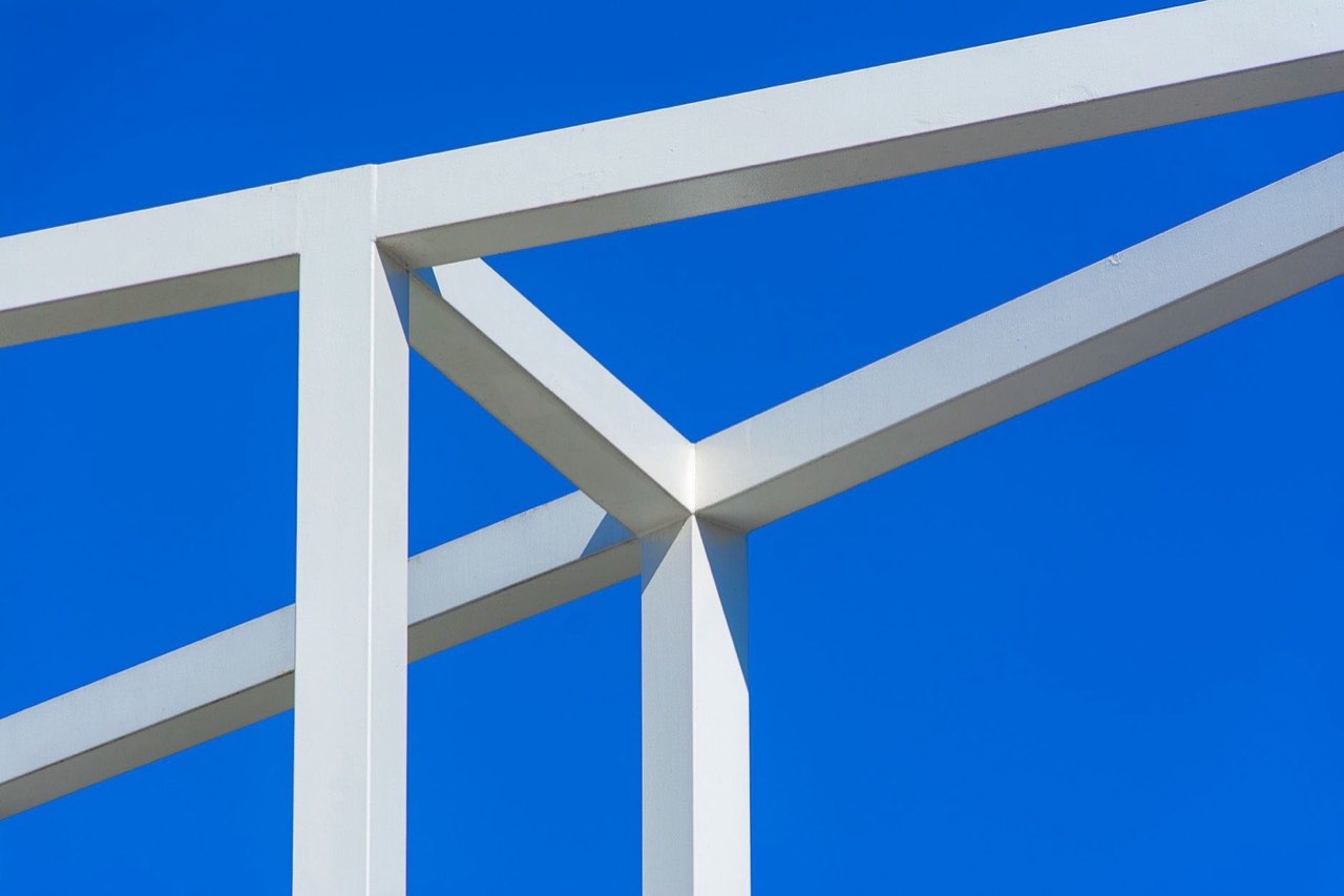White steel beams meeting at a joint against a clear blue sky
