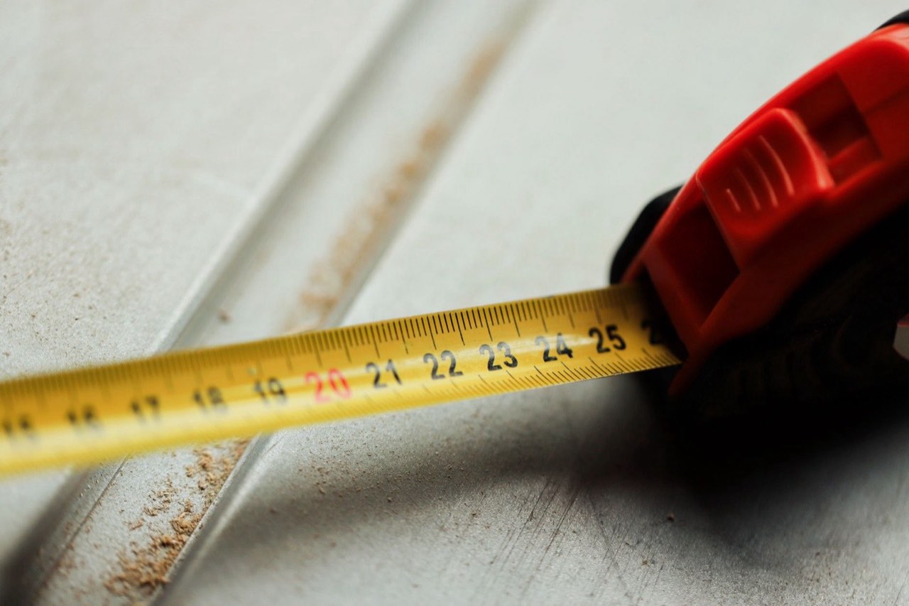 A tape measure pulled out across a scratched steel plate