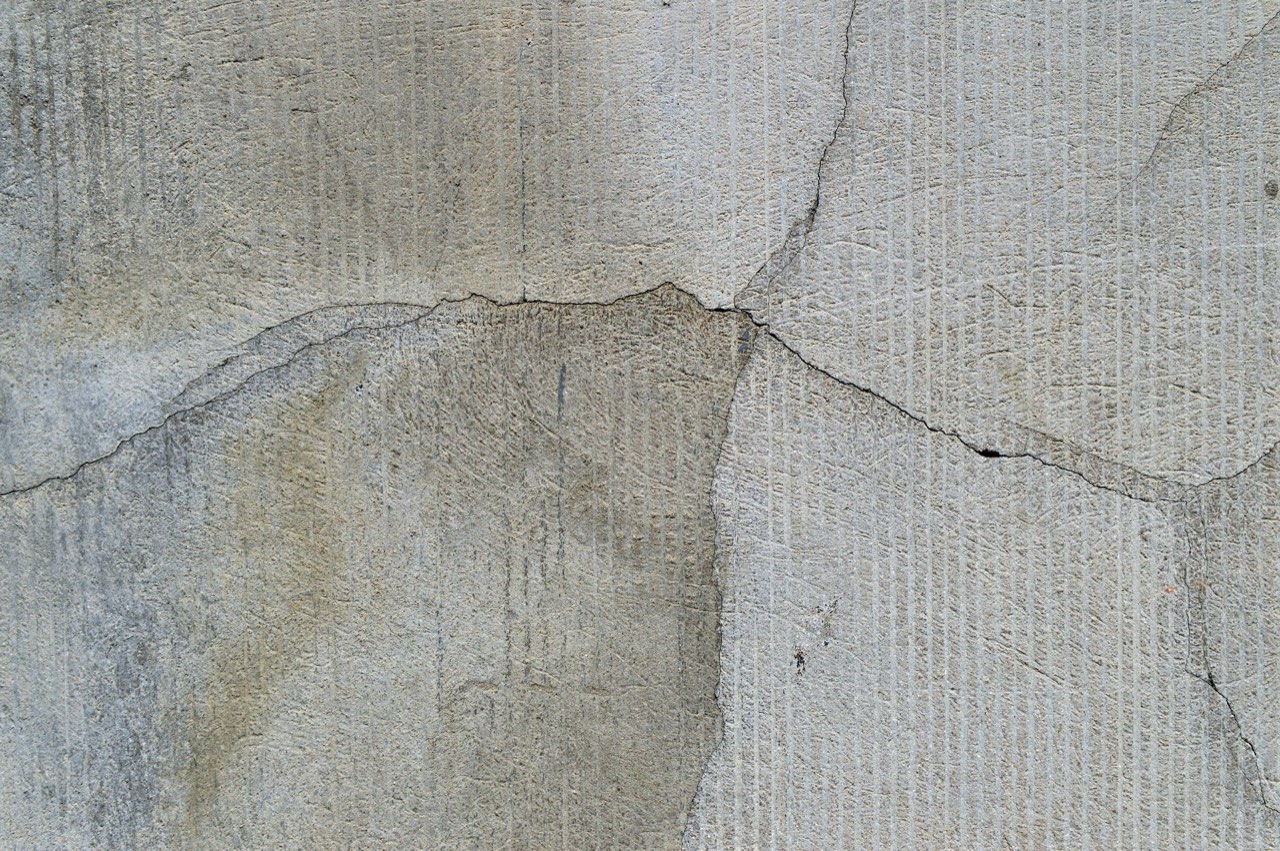 A grey rendered wall with branching cracks meeting near the middle and a darker damp patch below them