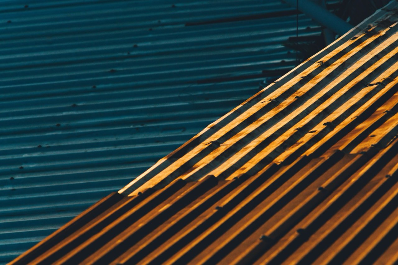 Two corrugated metal roof planes meeting at a ridge, one in blue shadow and the other lit orange by low sun